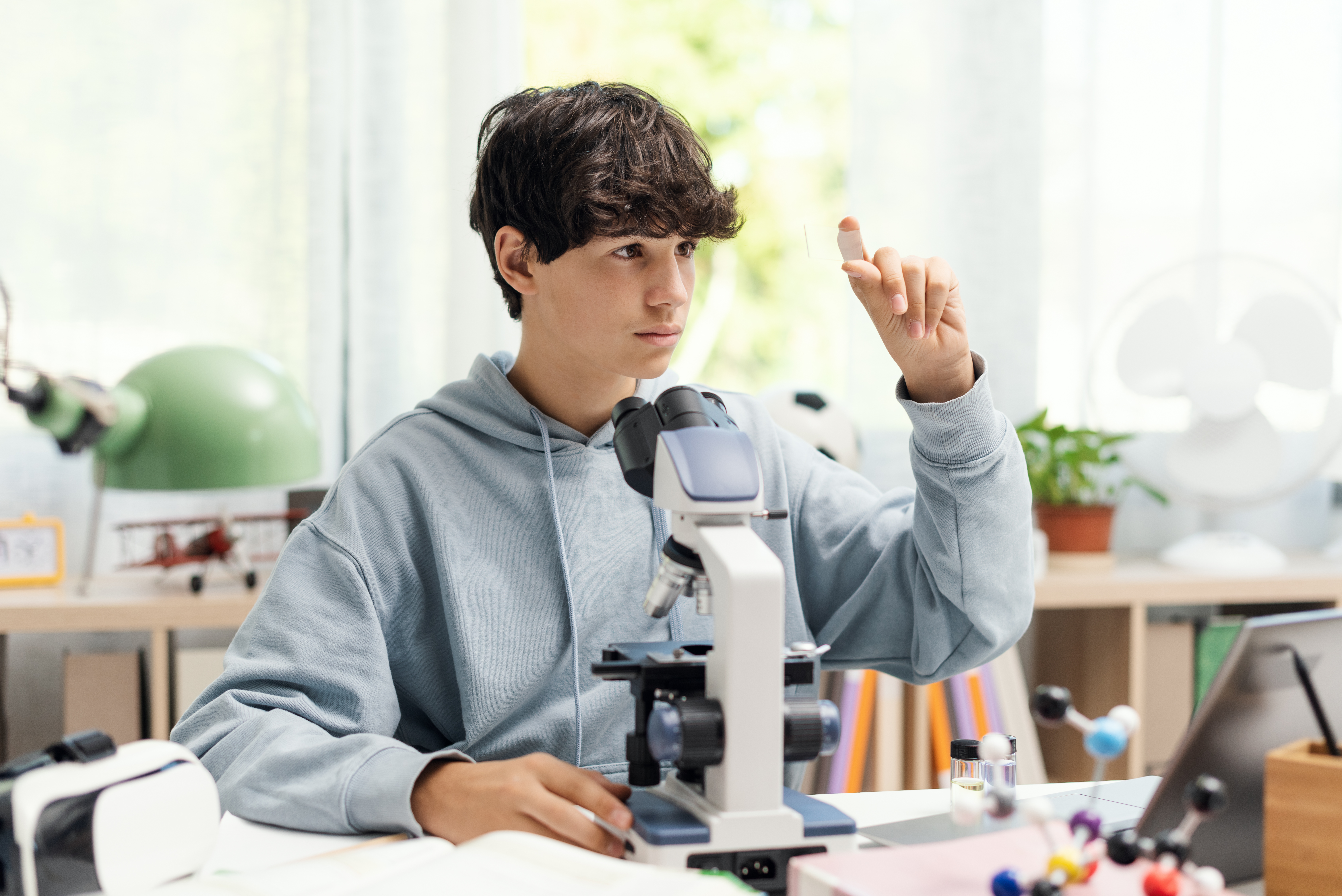 Student examining a specimen through a microscope at a desk in a bright science classroom
