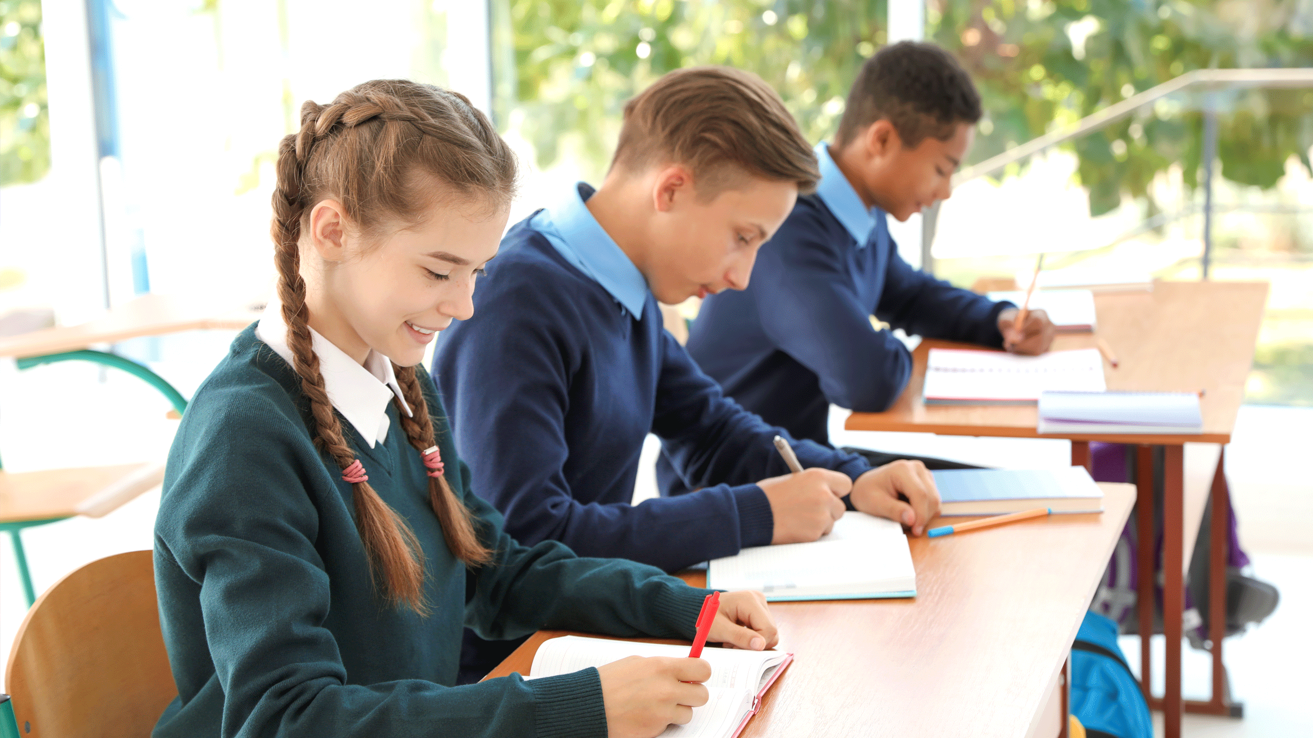 Mixed group of students making notes in a workbook sat at a desk.
