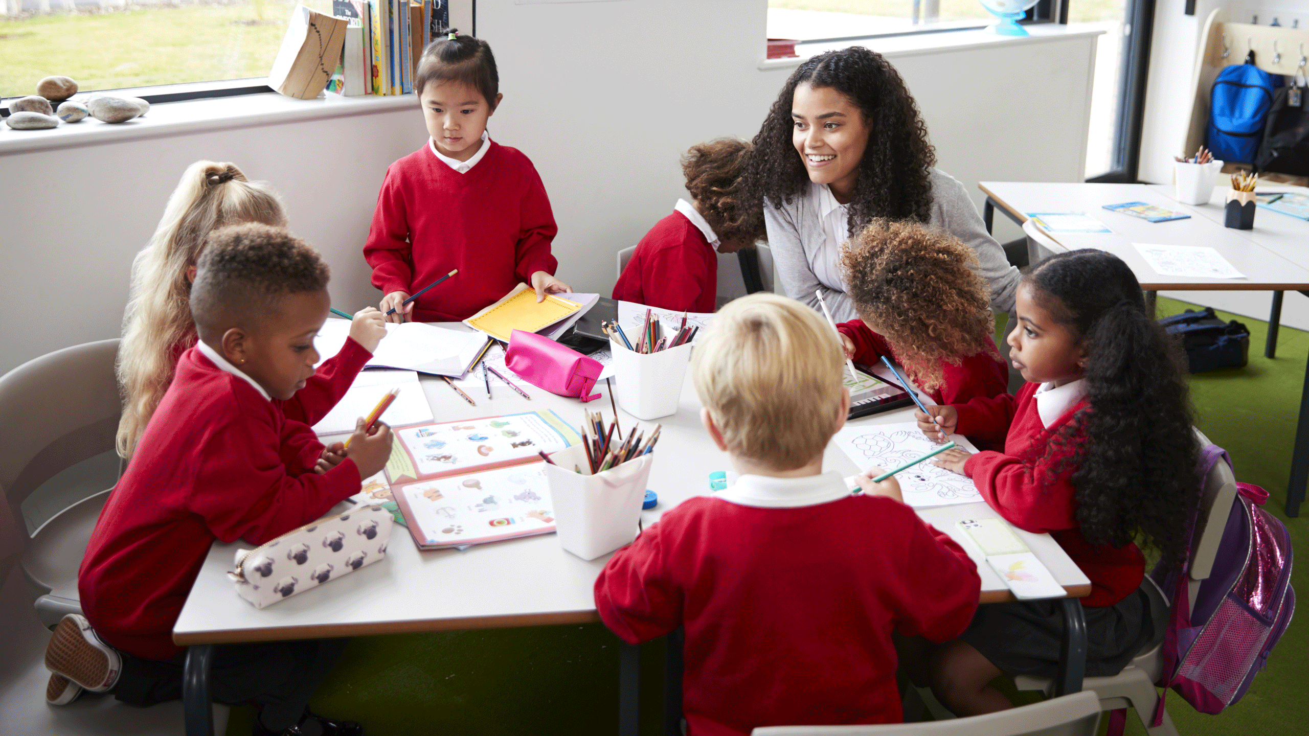 Teacher speaking with primary aged students around a classroom table. 