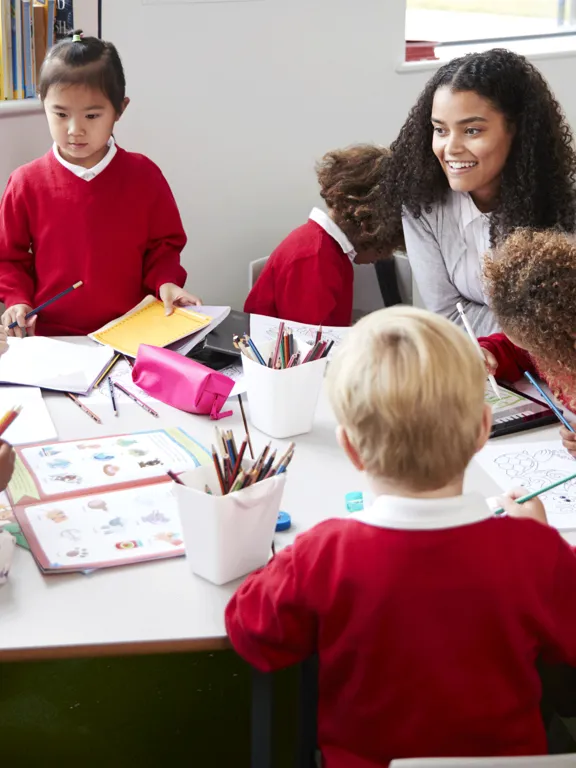 Teacher speaking with primary aged students around a classroom table.