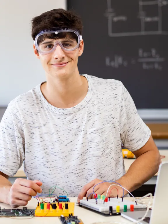 Student assembling electronic components and circuits on a desk in a physics classroom