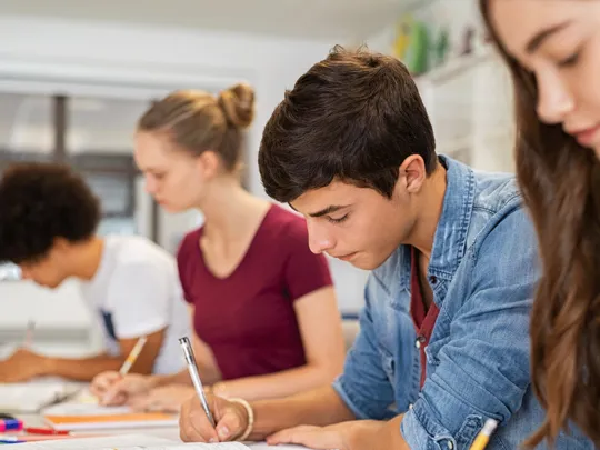 Mixed group of students writing into a text book.